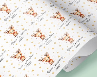 Op de afbeelding: Wit inpakpapier met een herhalend patroon van gouden sterren en een cartoon rendier met de tekst "Merry Christmas Harry" in gouden letters.