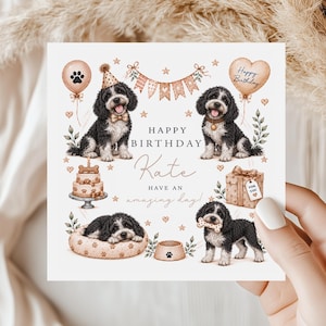 Könnte beinhalten: Eine quadratische Geburtstagskarte mit Illustrationen von schwarz-weißen Hunden, einer Torte, einem Geschenk und Luftballons. Der Text lautet: Happy Birthday Kate, have an amazing day! Das Design enthält Pfotenabdrücke, Sterne und Wimpel in sanften Beige- und Brauntönen.