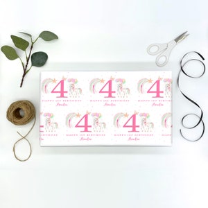 May include: White wrapping paper with a pink unicorn and rainbow design. The paper features the number "4" and the text "Happy 1st Birthday Amelia".