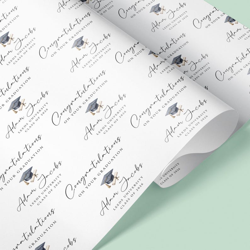 May include: White wrapping paper featuring a graduation design. The paper is printed with the name "Adam Jacobs", "Leeds University", and "Class of 2026", along with a graduation cap and scroll, ideal for gifts.