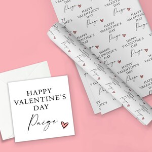 May include: White gift wrap with a repeating pattern of pink hearts and the text "Happy Valentine's Day Paige". A white card with the same text is also shown.