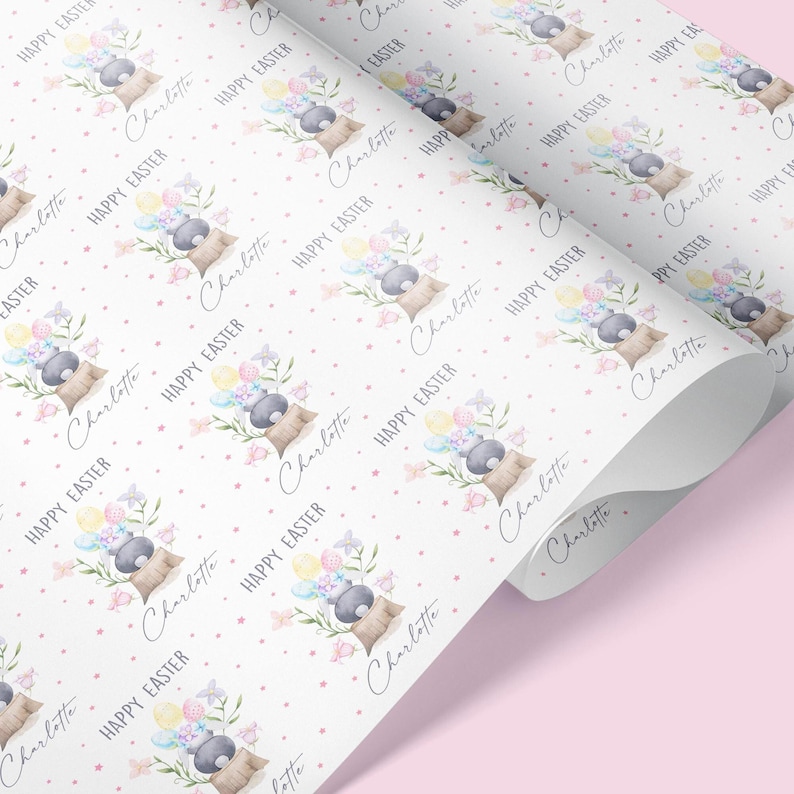 May include: White wrapping paper with a repeating pattern of a gray bunny holding pastel colored Easter eggs, pink flowers, and green leaves. The text "Charlotte" and "Happy Easter" is repeated throughout the pattern.