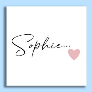 Pu&ograve; includere: Un biglietto bianco con il nome "Sophie..." scritto in corsivo nero e un cuore rosa.