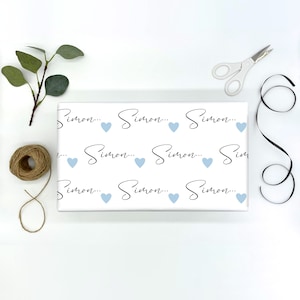Pu&ograve; includere: Carta da regalo bianca con un motivo ripetuto del nome "Simon..." in scrittura nera con un cuore blu chiaro tra ogni nome.