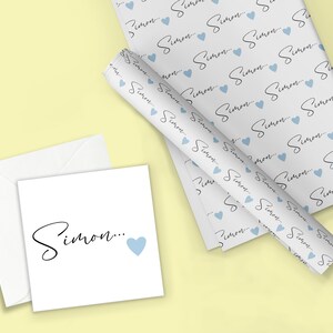 Pu&ograve; includere: Carta da regalo bianca con un motivo ripetuto del nome "Simon" in scrittura nera con un cuore blu chiaro dopo ogni nome. &Egrave; mostrata anche una carta bianca con il nome "Simon" in scrittura nera e un cuore blu chiaro.