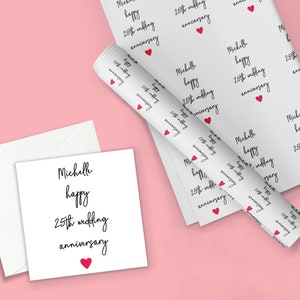 May include: White wrapping paper with a repeating pattern of the text "Michelle happy 25th wedding anniversary" and a small red heart. A white card with the same text and a red heart is shown next to the wrapping paper.