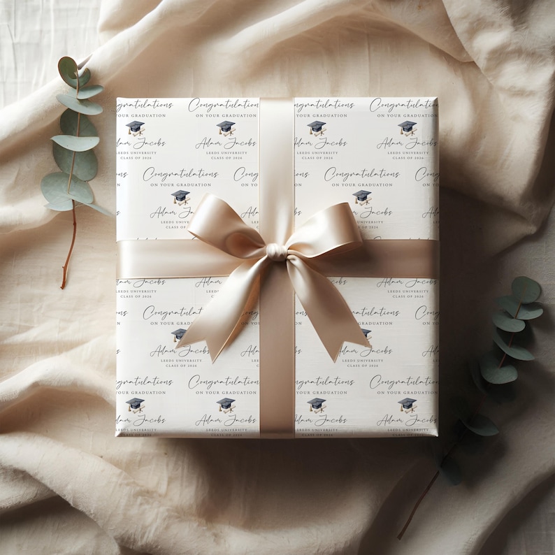 May include: A wrapped gift with graduation-themed wrapping paper. The paper is white with repeating text that reads "Congratulations on your graduation" and a graduation cap graphic. A cream-colored ribbon and bow are tied around the gift.