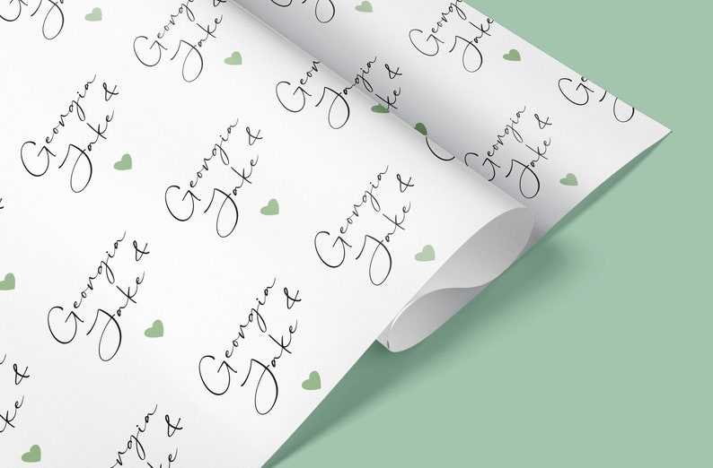 Pu&ograve; includere: Carta da regalo bianca con un motivo ripetuto dei nomi "Georgia & Jake" in elegante corsivo, intervallati da piccoli cuori verdi. La carta &egrave; parzialmente arrotolata.