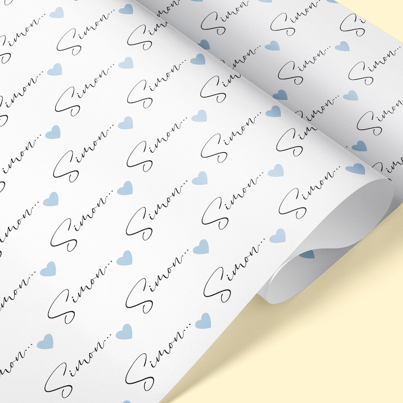 Pu&ograve; includere: Carta da regalo bianca con un motivo ripetuto di cuori blu chiaro e il nome "Simon..." scritto in corsivo nero.