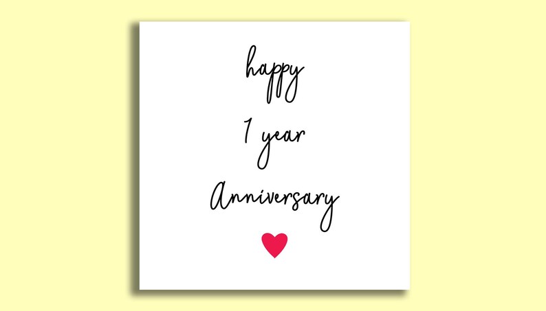 Op de afbeelding: Een witte vierkante kaart met de woorden "happy 1 year Anniversary" in zwart script. Onderaan staat een klein rood hart. De kaart staat op een lichtgele achtergrond.