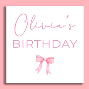 May include: A white card with pink text that reads "Olivia's Birthday" and a pink bow.