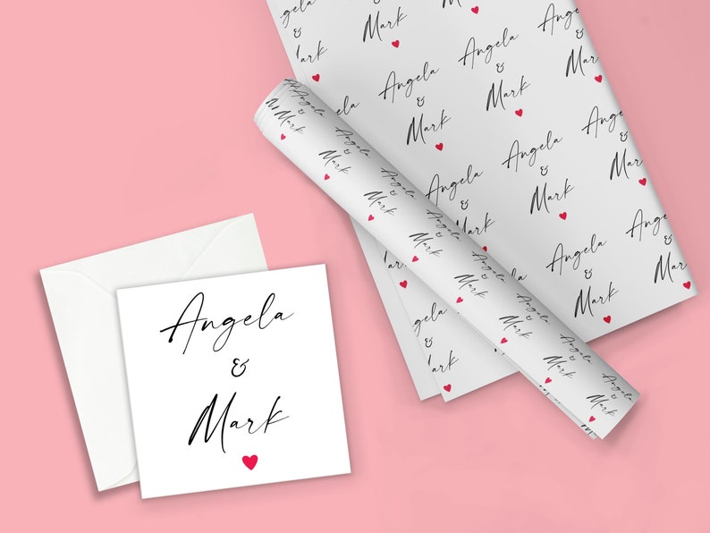 K&ouml;nnte beinhalten: Wei&szlig;es Geschenkpapier mit einem sich wiederholenden Muster der Namen "Angela & Mark" in schwarzer Schrift mit einem kleinen roten Herzen zwischen jedem Namen.