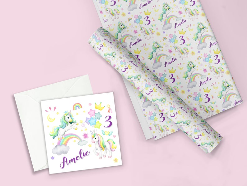 Op de afbeelding: Een witte kaart met een ontwerp van een eenhoorn en regenboog. De kaart heeft de naam "Amelie" en het nummer "3" erop. De kaart wordt vergezeld door een witte envelop.