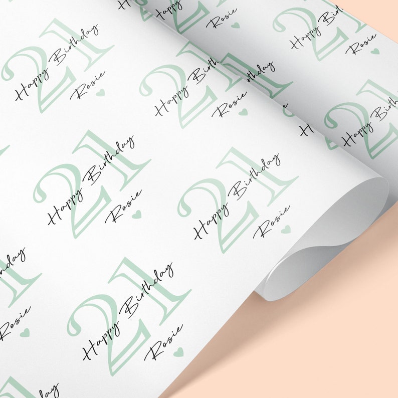 May include: White wrapping paper with a repeating pattern of the number 21 in a light green color, along with the words "Happy Birthday Rosie" in black script. Small green hearts are scattered throughout the design.