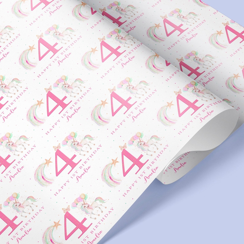 May include: White wrapping paper with a repeating pattern of pink unicorns, rainbows, stars, and the number 4. The text "Happy 1st Birthday Amelia" is repeated throughout the pattern.