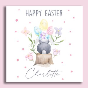 May include: A white card with a watercolor illustration of a bunny rabbit sitting on a tree stump with Easter eggs and flowers. The text "Happy Easter Charlotte" is printed on the card.
