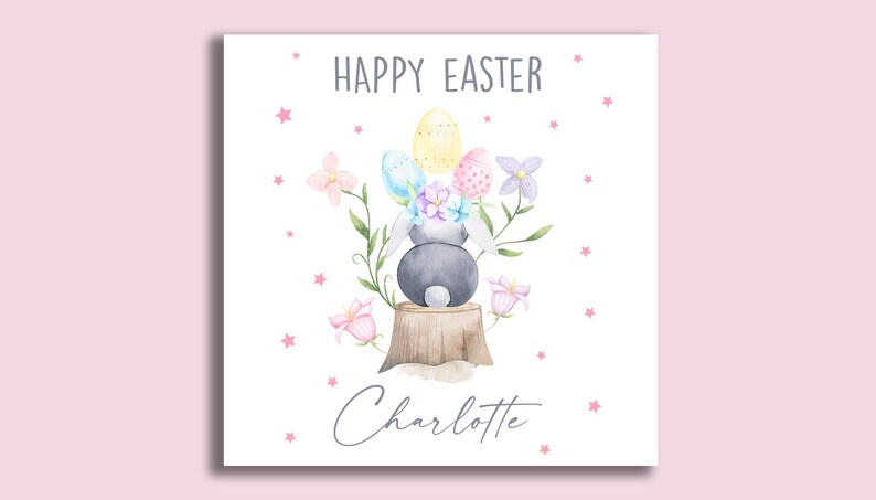May include: A white card with a watercolor illustration of a bunny rabbit sitting on a tree stump with Easter eggs and flowers. The text "Happy Easter Charlotte" is printed on the card.