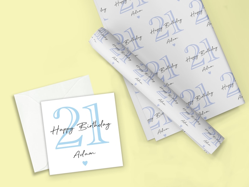 May include: A birthday gift set featuring a white card with a light blue "21 Happy Birthday Adam" design, a matching envelope, and wrapping paper with a repeating pattern of the same design. The wrapping paper is rolled up.