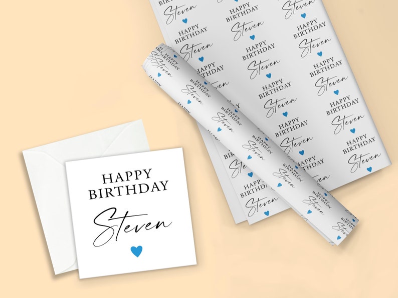 Pode incluir: Um cart&atilde;o de anivers&aacute;rio branco e um envelope a condizer com as palavras "HAPPY BIRTHDAY Steven" em escrita preta e um cora&ccedil;&atilde;o azul. Um rolo de papel de embrulho a condizer tamb&eacute;m &eacute; vis&iacute;vel, com o mesmo texto e design de cora&ccedil;&atilde;o.