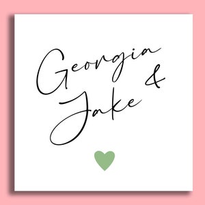 Pu&ograve; includere: Un biglietto quadrato bianco con i nomi "Georgia & Jake" in elegante scrittura nera. Un piccolo cuore verde &egrave; centrato sotto i nomi. Lo sfondo &egrave; rosa tenue.