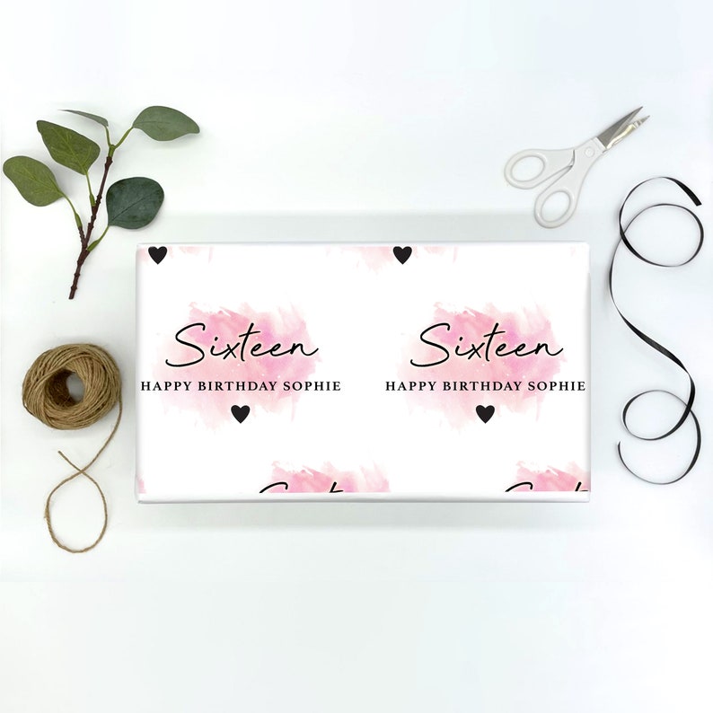 May include: White wrapping paper with a pink watercolor design and the text "Sixteen Happy Birthday Sophie" repeated. Black hearts are scattered throughout the design.