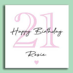 May include: A white birthday card with a light pink "21" and the words "Happy Birthday Rosie" in black script. A small pink heart is at the bottom. The card is on a light green background.