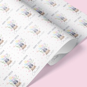 May include: White wrapping paper with a repeating pattern of a bunny holding balloons and flowers. The text "Happy Easter" and the name "Charlotte" are repeated throughout the pattern.