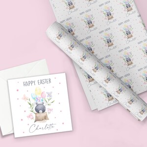 May include: A white card with a pink border and a watercolor illustration of a bunny holding colorful Easter eggs. The text "HAPPY EASTER" and the name "Charlotte" are printed on the card.