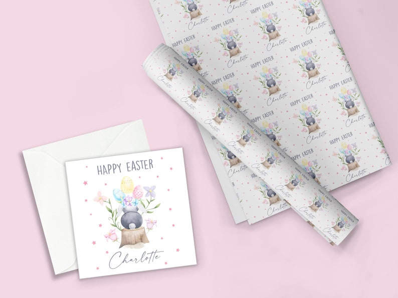 May include: A white card with a pink border and a watercolor illustration of a bunny holding colorful Easter eggs. The text "HAPPY EASTER" and the name "Charlotte" are printed on the card.