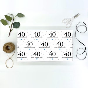May include: White wrapping paper with a repeating pattern of black polka dots, blue hearts, and the number 40. The text "Happy Birthday James" is repeated throughout the pattern.