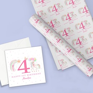 May include: A white card with a pink number four, a rainbow, a star, and a unicorn with balloons. The text reads "Happy 1st Birthday Amelia". The card is on a white envelope. A roll of wrapping paper with a repeating pattern of pink number fours, rainbows, stars, and unicorns with balloons. The text on the wrapping paper reads "Happy 1st Birthday Amelia".