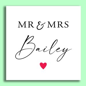 Op de afbeelding: Een witte vierkante kaart met de tekst "MR & MRS Bailey" in zwart script en een klein rood hartje onderaan. De achtergrond is lichtgroen.