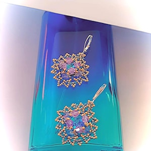May include: A pair of earrings with a blue and purple flower design. The earrings are made with small beads and have a silver hook.