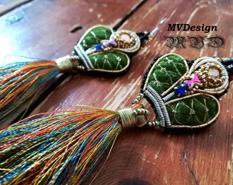 Puede incluir: Un par de pendientes de terciopelo verde con adornos dorados y plateados, con un diseño de corona y cuentas de colores. Los pendientes tienen borlas largas y multicolores.