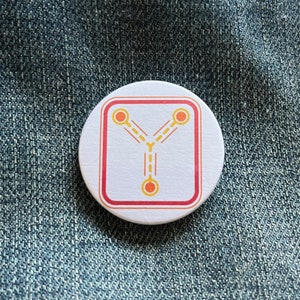May include: A white round button with a red border and a yellow stylized symbol inside. The symbol is a Y shape with three circles at the ends of the arms.