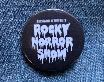 May include: A black button with white text that reads "Richard O'Brien's Rocky Horror Show" with the letters dripping down the button.