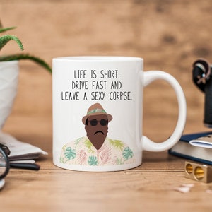 May include: White ceramic mug with the quote: "LIFE IS SHORT. DRIVE FAST AND LEAVE A SEXY CORPSE." The mug has a cartoon illustration of a man in sunglasses and a Hawaiian shirt. A humorous gift idea for a friend.