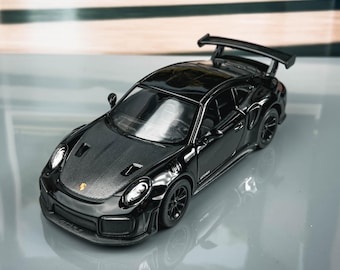 May include: A black model car with a rear spoiler. The miniature vehicle has detailed features, including headlights and wheels. The car is displayed on a reflective surface. The model is a miniature replica.