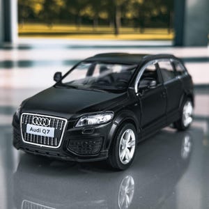 Puede incluir: Un coche modelo Audi Q7 negro con ruedas plateadas. La parte delantera del coche muestra el logotipo de Audi y el texto "Audi Q7" en una parrilla plateada. Es un SUV en miniatura.