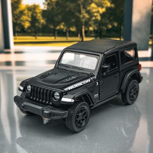 May include: A black Jeep Rubicon model car with black wheels and a black roof. The word "RUBICON" is printed on the hood. The model is a miniature replica of a Jeep.