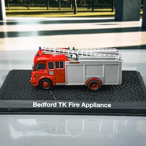 May include: A detailed model of a Bedford TK Fire Appliance, with a red cab and silver body. It has a ladder on top and is mounted on a black base. The text "Bedford TK Fire Appliance" is visible.