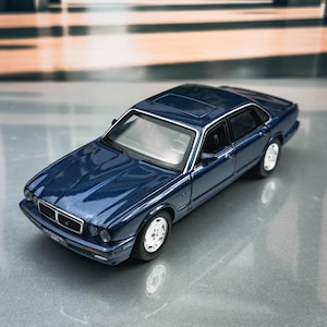 Könnte beinhalten: Ein Miniaturmodell eines dunkelblauen Jaguar-Limousinen mit Schiebedach. Das Spielzeugauto hat silberne Felgen und schwarze Fenster. Das Modell steht auf einer reflektierenden Oberfläche mit unscharfem Hintergrund.