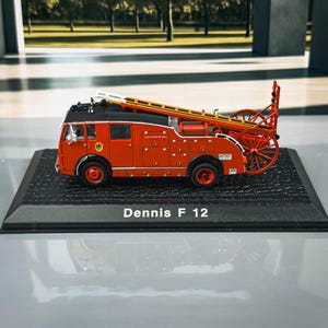 May include: A miniature red fire engine model with a black roof and a yellow ladder. The model has red wheels and a black base. The text "Dennis F 12" is printed on the base.
