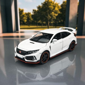 Könnte beinhalten: Ein weißes Modellauto mit schwarzen und roten Akzenten. Das Auto hat schwarze Räder mit roter Zierleiste und einen Heckspoiler. Das Auto ist ein Schrägheck mit einem schlanken Design.