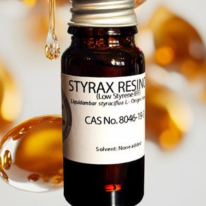 May include: A small, dark amber glass bottle with a silver cap. The label reads "STYRAX RESIN" and includes details about the product's origin and composition. The image features a close-up of the bottle with a blurred background and a golden liquid.