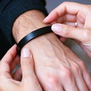 Op de afbeelding: Een eenvoudige, effen zwarte armband met een gladde, matte afwerking. De band heeft een uniforme breedte en een strak ontwerp dat om de pols sluit, wat zorgt voor een elegante en ingetogen uitstraling voor dagelijks gebruik.