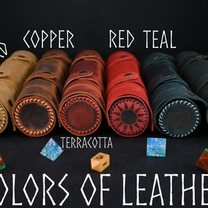 May include: Six leather dice rolling tubes in different colors: mustard, copper, terracotta, red, teal, and green. The tubes are lined up in a row and have a sun design on the end. The text "Colors of Leather" is written below the tubes.