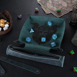 May include: A green felt dice tray with a black and white illustration of a mythical creature. The tray is filled with blue and green dice. A green leather dice rolling tube with a zipper is also included.