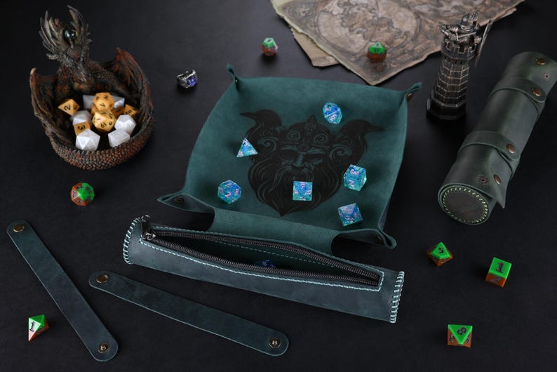 May include: A green felt dice tray with a black and white illustration of a mythical creature. The tray is filled with blue and green dice. A green leather dice rolling tube with a zipper is also included.
