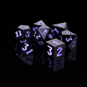 Könnte beinhalten: Ein Satz schwarzer Würfel mit violetten Zahlen. Die Würfel sind aus einem glatten, polierten Material gefertigt und haben eine scharfe, eckige Form. Die Zahlen auf den Würfeln sind klar und leicht zu lesen.